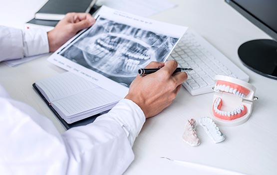 Male doctor or dentist writing report working with tooth x-ray film, model and equipment used in the treatment of dental and dentistry at workplace